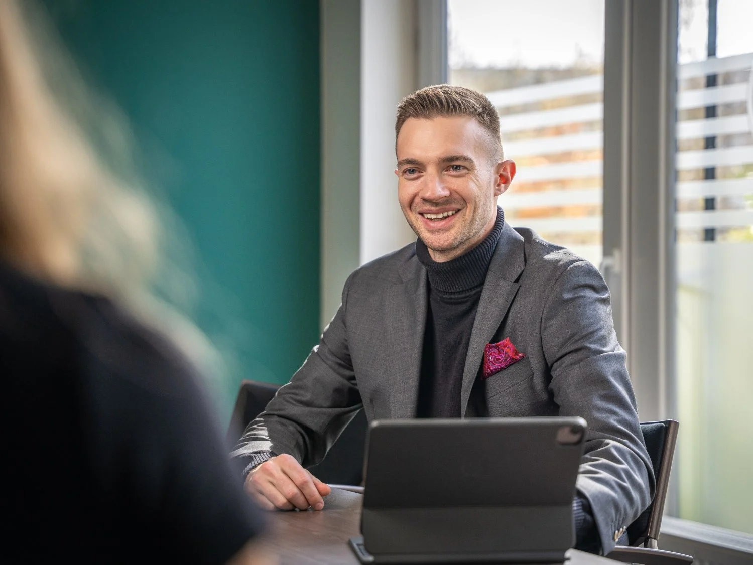 Steuerberater Patrick Herzer lächelt freundlich während eines Beratungsgesprächs mit einer Mandantin im Büro