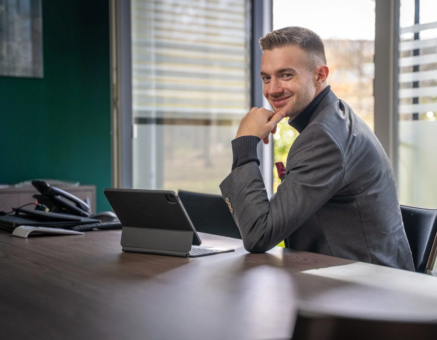 Steuerberater Patrick Herzer sitzt selbstbewusst an seinem modernen Schreibtisch mit einem Tablet