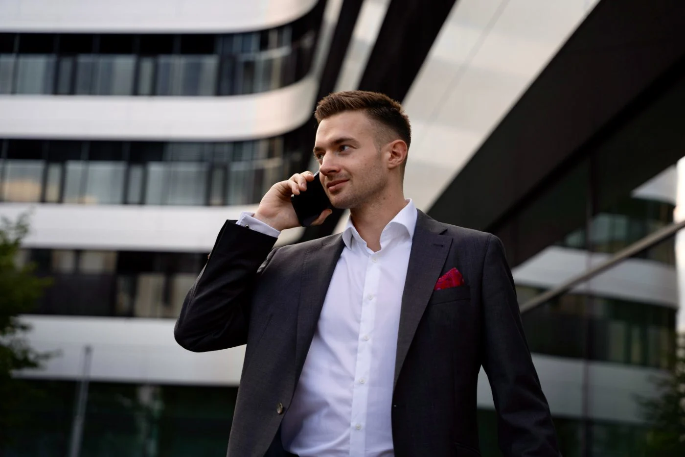 Steuerberater Patrick Herzer führt ein geschäftliches Telefonat mit dem Smartphone vor dem modernen Kanzleigebäude